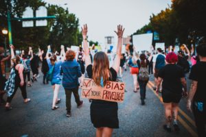 Una persona blanca con un cartel en el que pone "tu sesgo" y "tu privilegio" refiriéndose a los sesgos creados por la fragilidad blanca y la tendencia a negar nuestras emociones y aquello que no nos conviene.